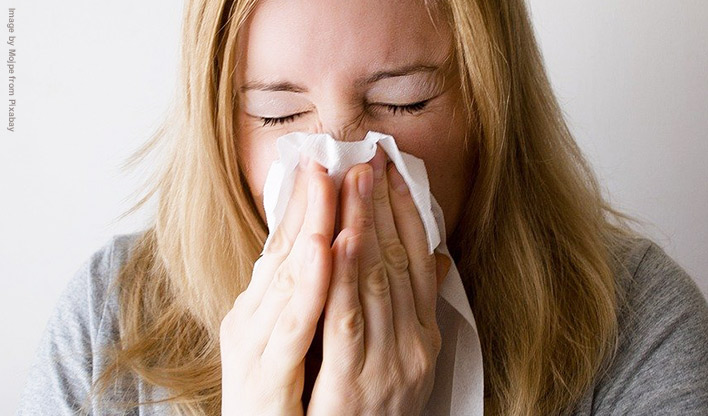 Blonde haired lady sneezing with a tissue.