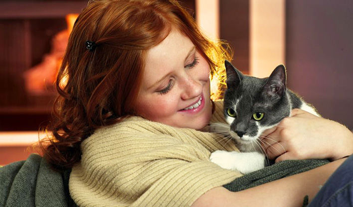 Cuddling a cat Red haired lady cuddling a grey and white cat while relaxing.